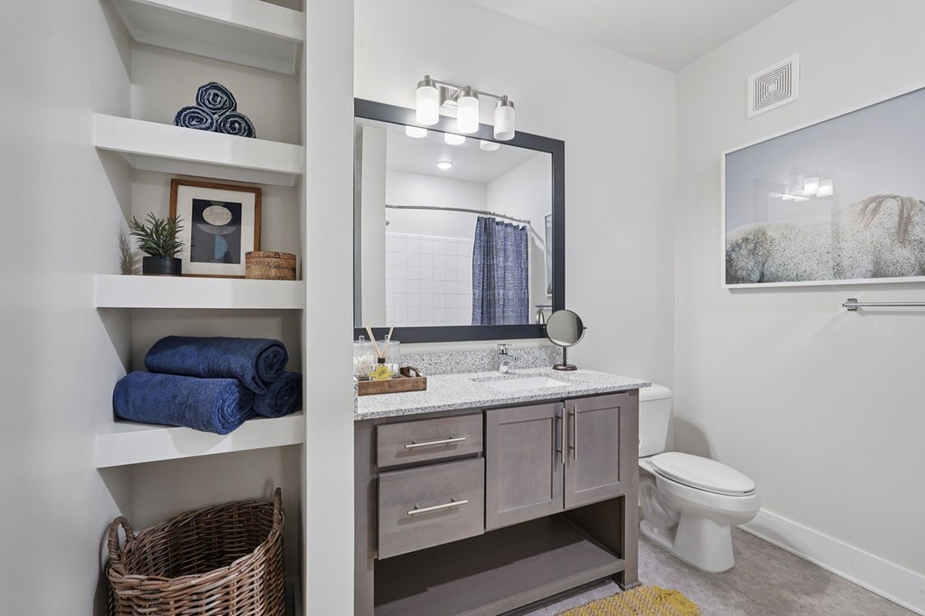 A bathroom with a toilet, sink, shower, and built-in shelving.